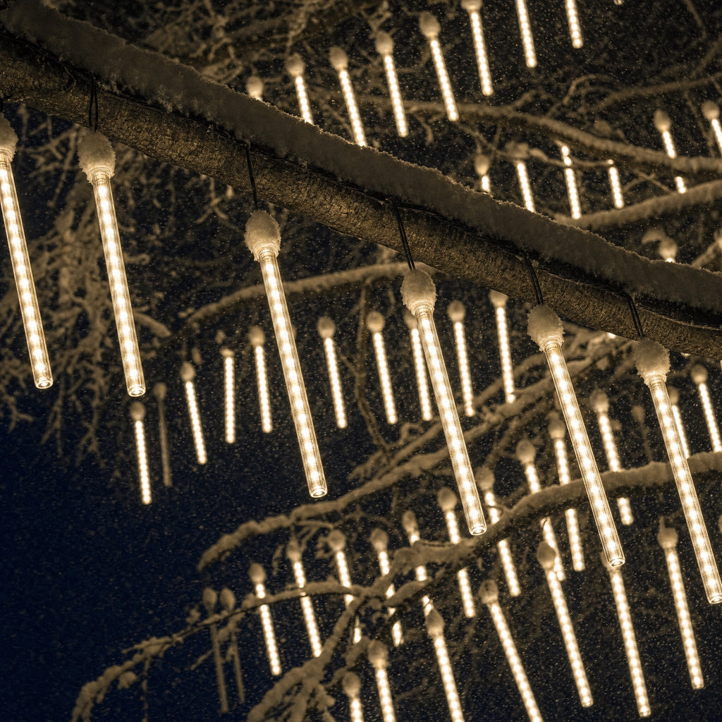 Warm white meteor lights hanging from a snow-covered branch at night